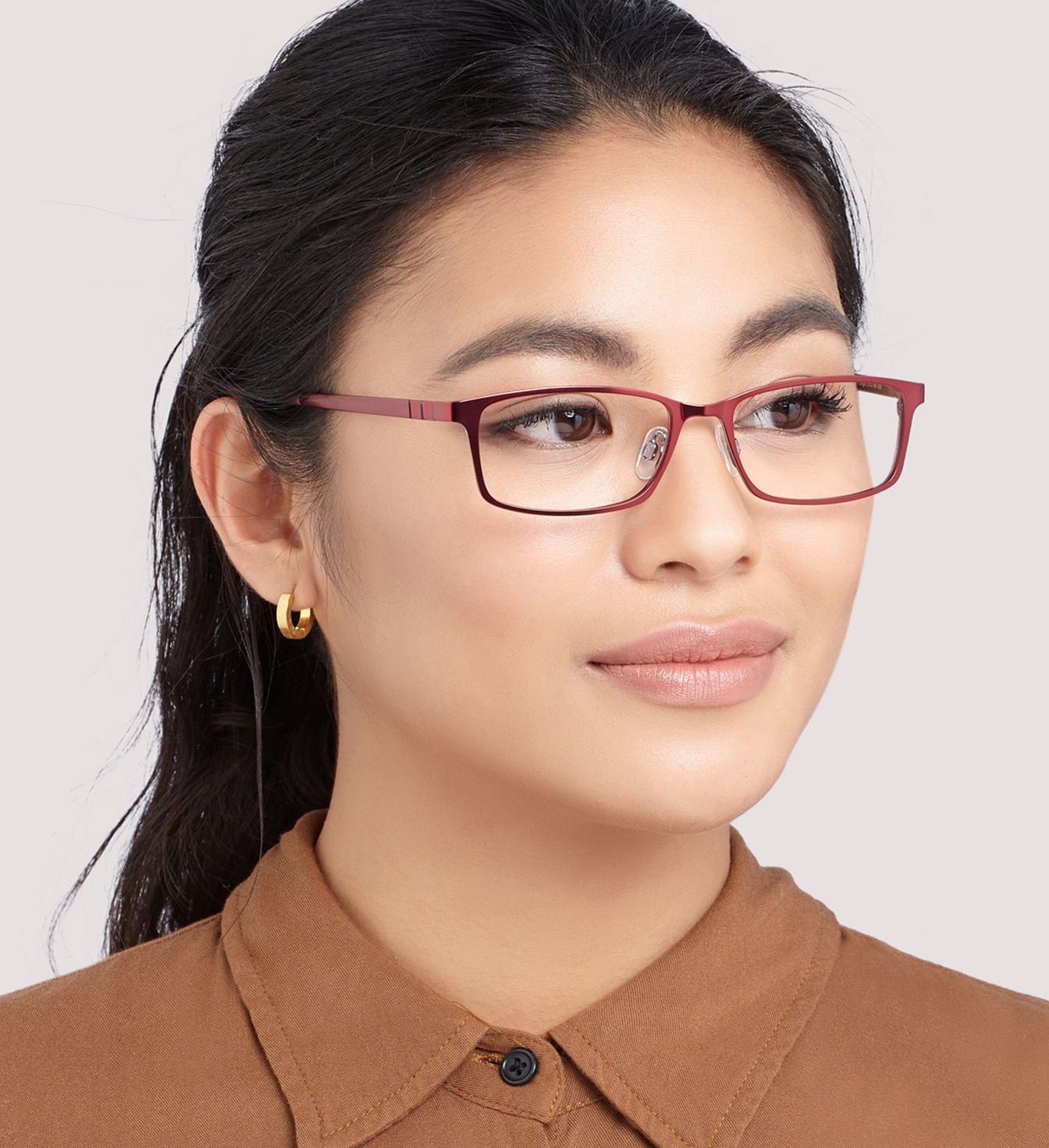A young lady with black hair tied back in a ponytail. She is wearing a shiny pair of pink metal rectangular glasses and smiles very gently.