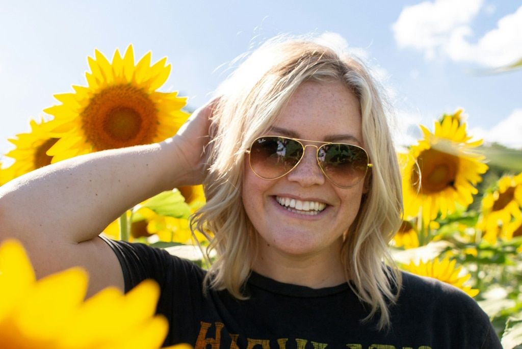 Smiling blonde woman wearing aviator sunglasses in a field of sunflowers