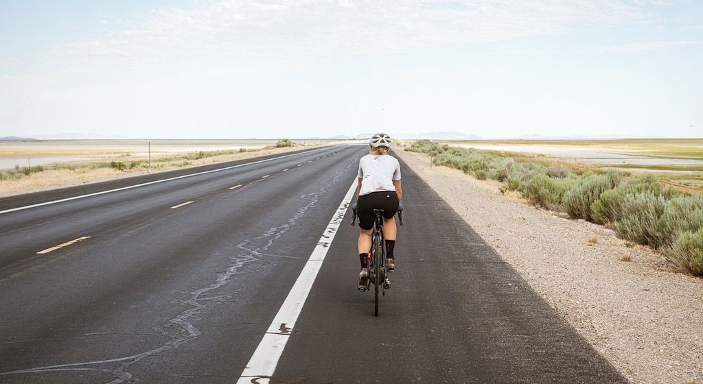 A cyclist from behind, riding along an empty road in the desert