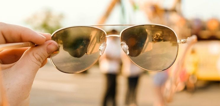 A hand holding up aviator sunglasses in front of a blurry backdrop