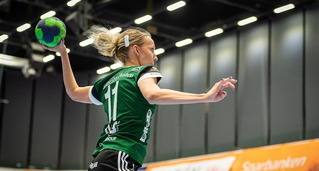A blonde woman in a green jersey about to throw the ball in handball