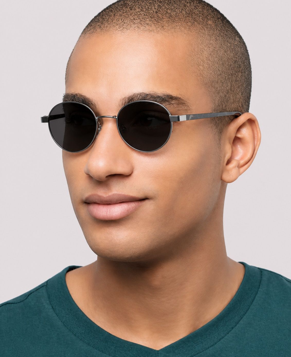 A smiling man with shaved hair wears a green t-shirt and The Collection Cody silver metal sunglasses with tortoiseshell temples, posed against a clean white background.