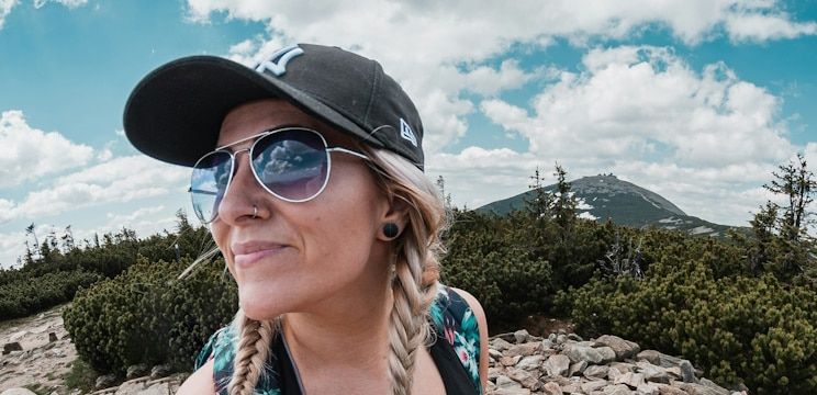 A woman with blonde braids wearing a cap and aviator sunglasses while being active outdoors