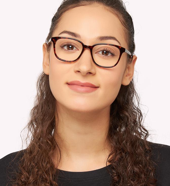 A woman with long brown hair that's hanging in waves over her shoulders, with the sides tied behind her head. She's wearing Kate Spade Bari glasses.