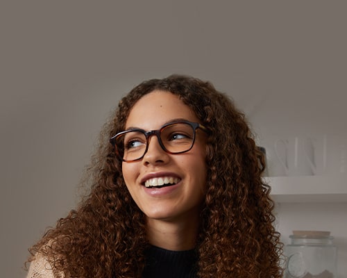 A smiling woman with long curly hair, wearing tortoiseshell glasses frames