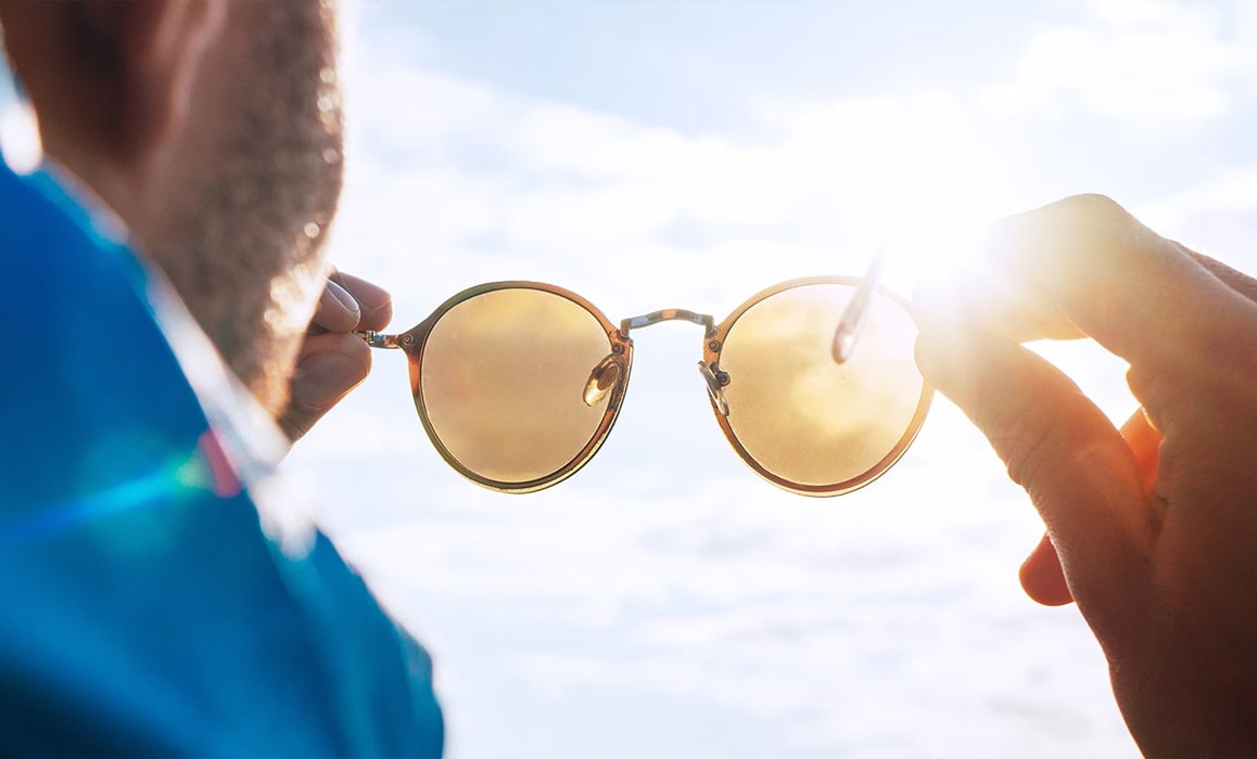 A man holding a pair of sunglasses up to the sun