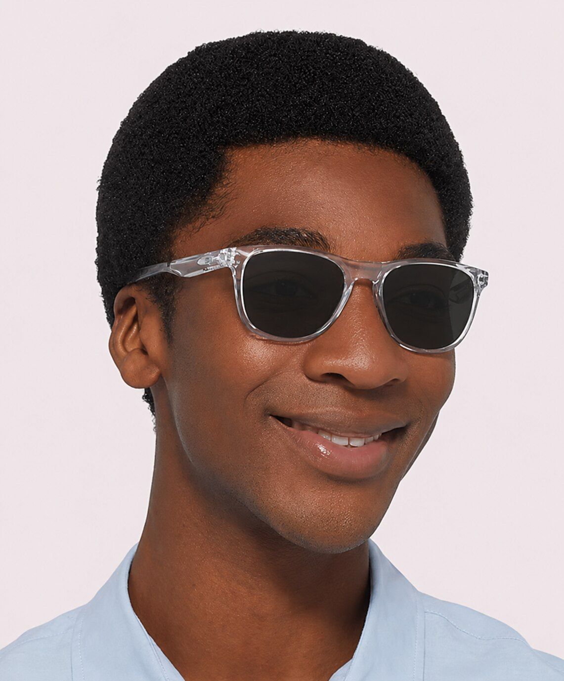 Man with short afro wearing a light-blue shirt and round polished clear Oakley Trillbe™ X  prescription sunglasses against a light background.
