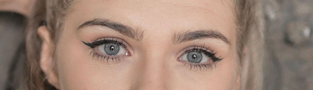 Close-up of a pale, blonde woman's face, highlighting the long lashes around her grey eyes.