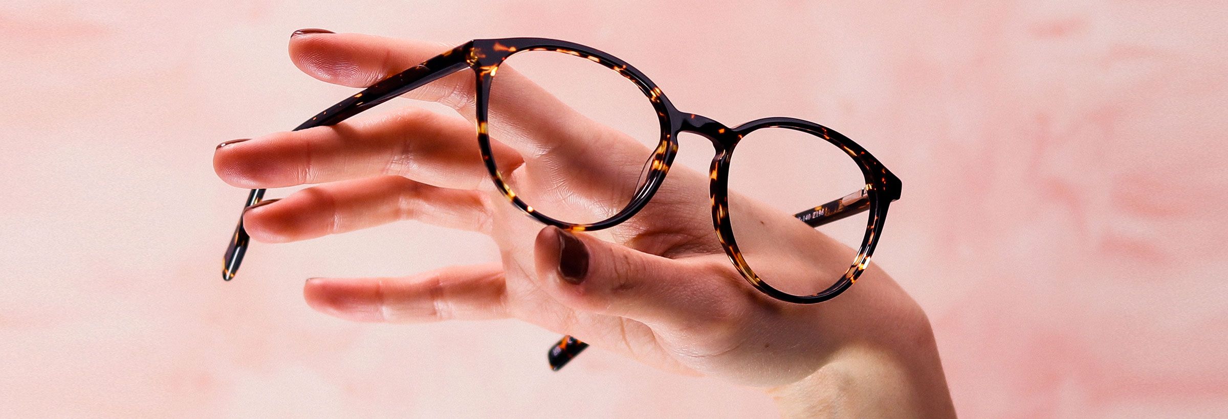 Woman's hand holding a pair of round tortoiseshell Pink Ribbon frames through her fingers