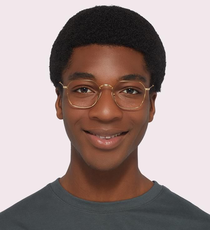 Image showing a man wearing hexagonal gold wire frames on a light pink background.