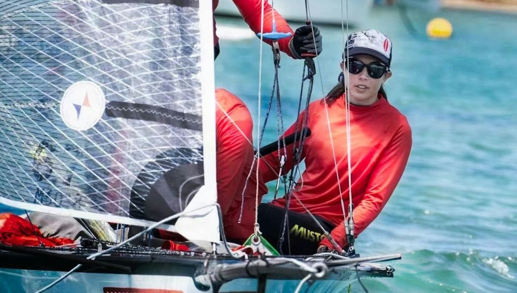 A woman in red leaning off the side of a sail boat while taking part in a race with her team