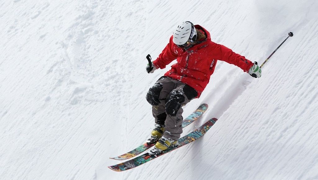 A skier in a red coat and a white helmet racing down a steep mountain slope