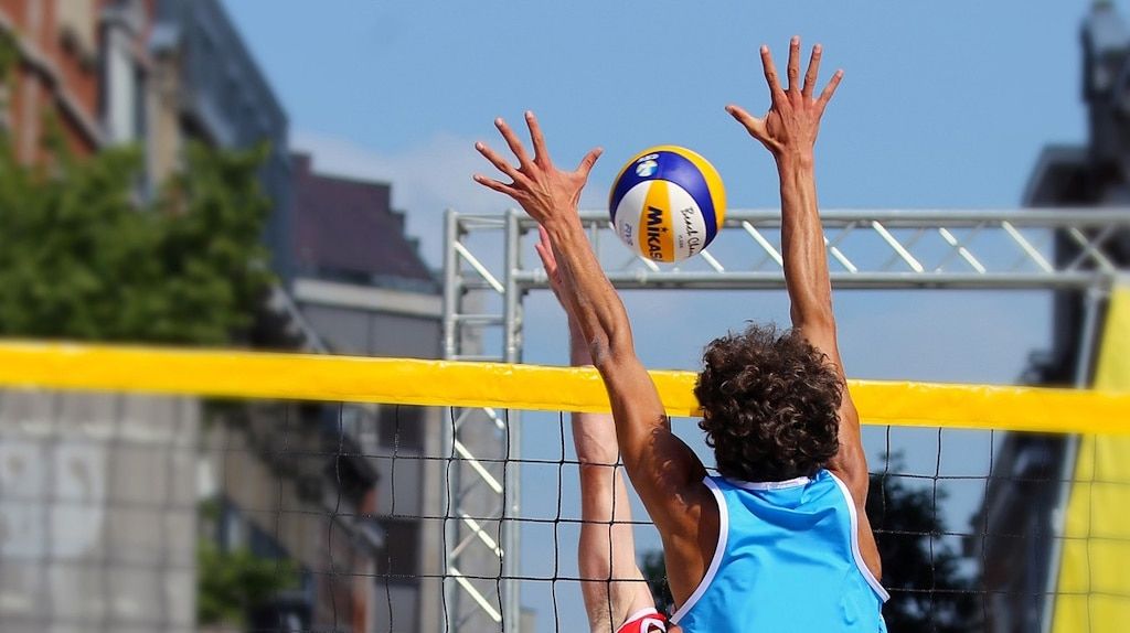 Two people jumping on opposite sides of a volleyball net in an effort to hit the ball